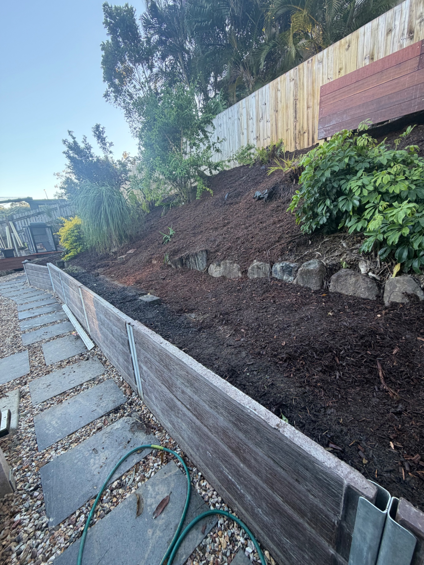 Hardwood sleeper garden retaining wall beside a paved stepping-stone path with freshly mulched garden beds