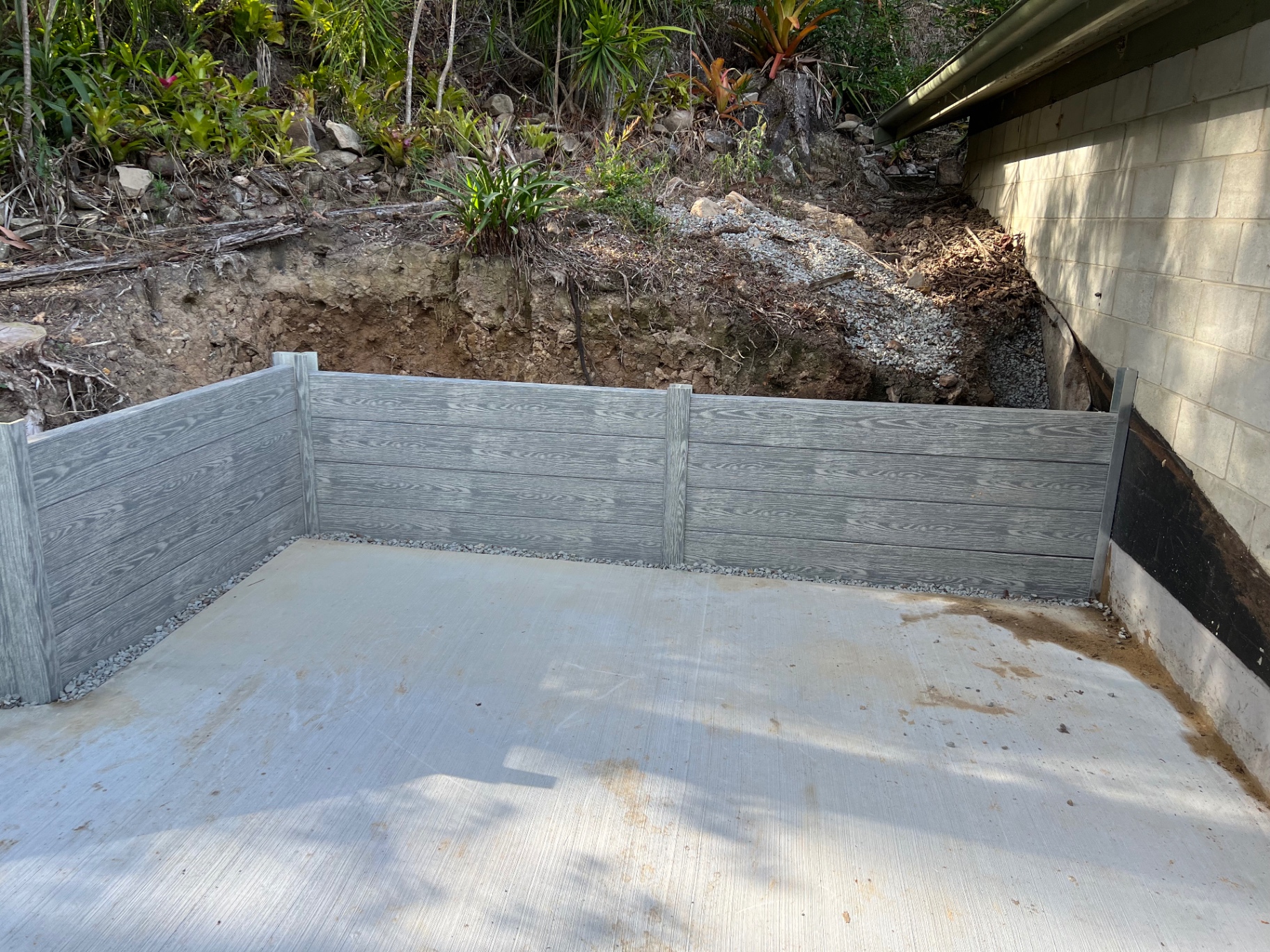 Grey concrete sleeper retaining wall with steel posts wrapping a new concrete slab beside a block wall