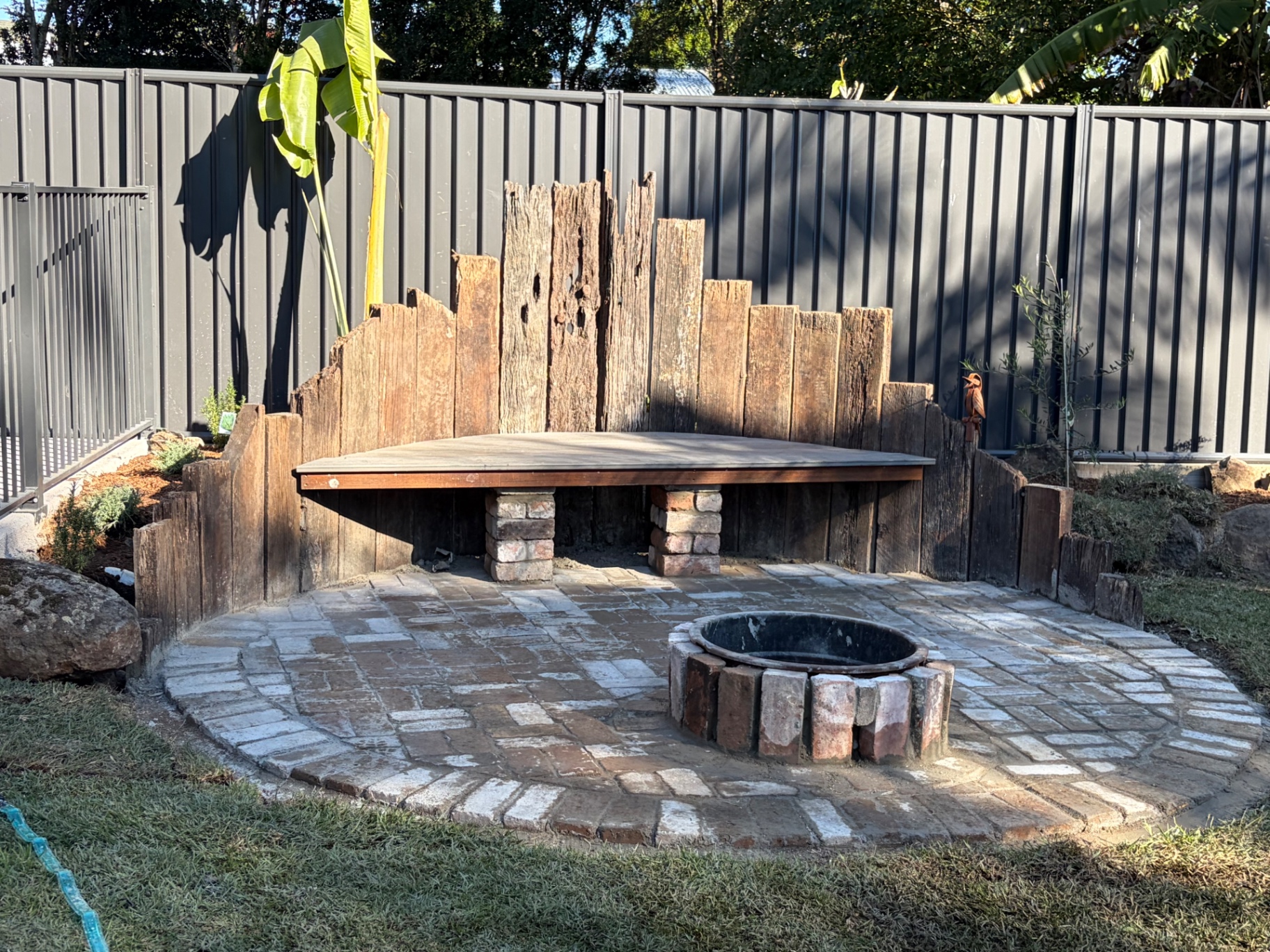Rustic timber fire pit seating area with reclaimed sleeper walls and paved stone patio in a Gold Coast backyard